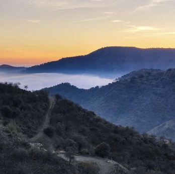 Sunset over misty mountain ridges with a winding path through the hills