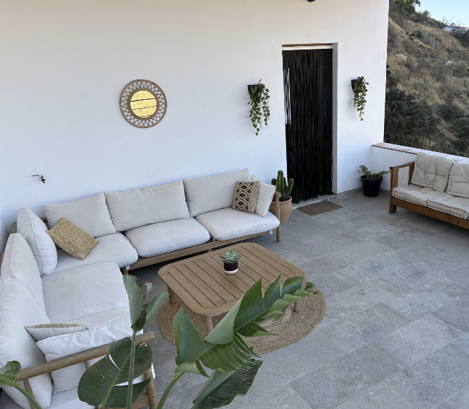 Terrace lounge with cream sofas, rattan mirror and plants against a white villa wall